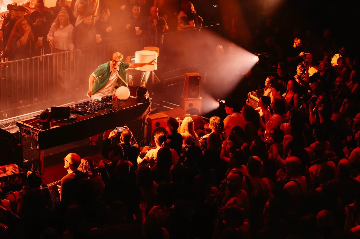 Owen Cutts DJing from a platform in the middle of the crowd at Outernet London, lit orange through haze