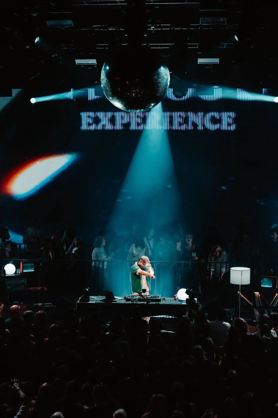 Owen Cutts under a single teal beam and a mirror ball, Experience on the LED wall behind